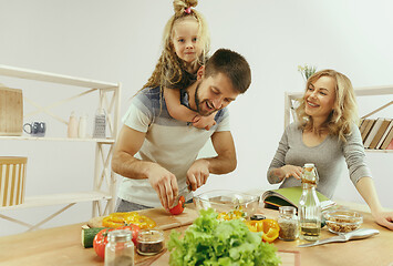 Image showing Cute little girl and her beautiful parents are cutting vegetables in kitchen at home