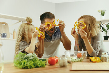 Image showing Cute little girl and her beautiful parents are cutting vegetables in kitchen at home