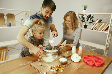 Image showing Cute little girl and her beautiful parents preparing the dough for the cake in kitchen at home