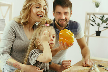 Image showing Cute little girl and her beautiful parents are cutting vegetables in kitchen at home