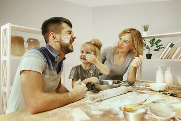 Image showing Cute little girl and her beautiful parents preparing the dough for the cake in kitchen at home