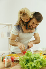 Image showing Cute little girl and her beautiful parents are cutting vegetables in kitchen at home