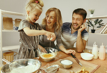 Image showing Cute little girl and her beautiful parents preparing the dough for the cake in kitchen at home