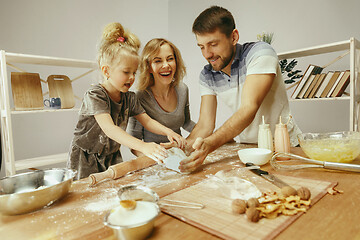 Image showing Cute little girl and her beautiful parents preparing the dough for the cake in kitchen at home