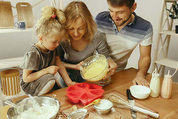 Image showing Cute little girl and her beautiful parents preparing the dough for the cake in kitchen at home