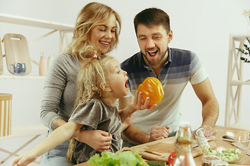 Image showing Cute little girl and her beautiful parents are cutting vegetables in kitchen at home