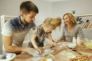 Image showing Cute little girl and her beautiful parents preparing the dough for the cake in kitchen at home