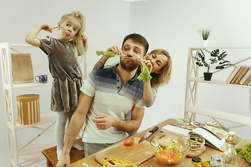 Image showing Cute little girl and her beautiful parents are cutting vegetables in kitchen at home