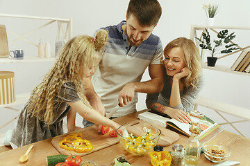 Image showing Cute little girl and her beautiful parents are cutting vegetables in kitchen at home