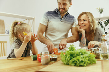 Image showing Cute little girl and her beautiful parents are cutting vegetables in kitchen at home