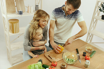 Image showing Cute little girl and her beautiful parents are cutting vegetables in kitchen at home