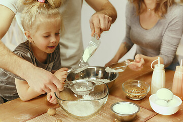 Image showing Cute little girl and her beautiful parents preparing the dough for the cake in kitchen at home