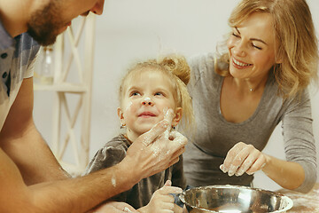 Image showing Cute little girl and her beautiful parents preparing the dough for the cake in kitchen at home