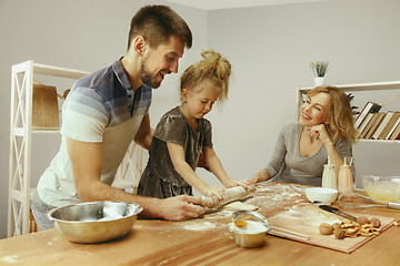 Image showing Cute little girl and her beautiful parents preparing the dough for the cake in kitchen at home