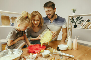 Image showing Cute little girl and her beautiful parents preparing the dough for the cake in kitchen at home