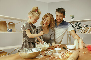 Image showing Cute little girl and her beautiful parents preparing the dough for the cake in kitchen at home