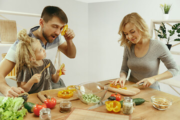 Image showing Cute little girl and her beautiful parents are cutting vegetables in kitchen at home