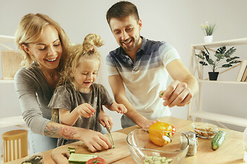 Image showing Cute little girl and her beautiful parents are cutting vegetables in kitchen at home