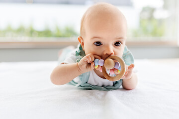 Image showing baby girl on white blanket chewing wooden rattle
