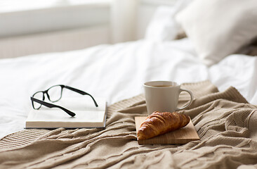 Image showing coffee, croissant, blanket and book on bed at home