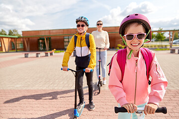 Image showing happy school children with mother riding scooters