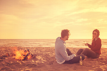 Image showing Young Couple Sitting On The Beach beside Campfire drinking beer