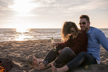 Image showing Young Couple Sitting On The Beach beside Campfire drinking beer