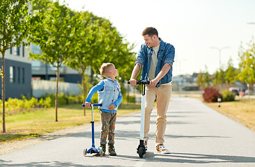 Image showing father and little son riding scooters in city