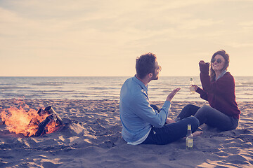 Image showing Young Couple Sitting On The Beach beside Campfire drinking beer