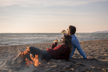 Image showing Young Couple Sitting On The Beach beside Campfire drinking beer