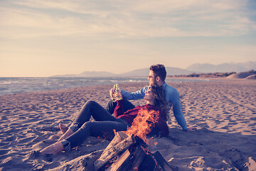 Image showing Young Couple Sitting On The Beach beside Campfire drinking beer