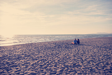 Image showing Young Couple Sitting On The Beach beside Campfire drinking beer