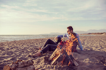 Image showing Young Couple Sitting On The Beach beside Campfire drinking beer