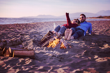 Image showing Young Couple Sitting On The Beach beside Campfire drinking beer