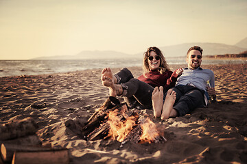 Image showing Young Couple Sitting On The Beach beside Campfire drinking beer