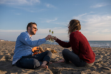 Image showing Young Couple Sitting On The Beach beside Campfire drinking beer