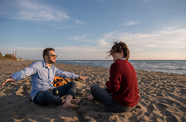 Image showing Young Couple Sitting On The Beach beside Campfire drinking beer