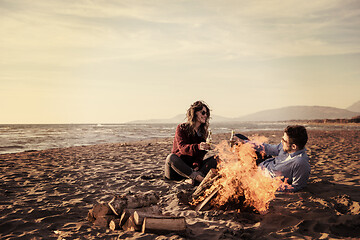 Image showing Young Couple Sitting On The Beach beside Campfire drinking beer