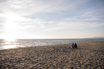 Image showing Young Couple Sitting On The Beach beside Campfire drinking beer