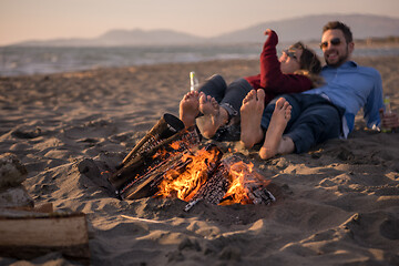 Image showing Young Couple Sitting On The Beach beside Campfire drinking beer