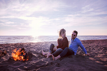 Image showing Young Couple Sitting On The Beach beside Campfire drinking beer