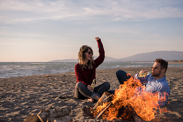 Image showing Young Couple Sitting On The Beach beside Campfire drinking beer