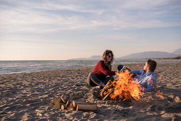 Image showing Young Couple Sitting On The Beach beside Campfire drinking beer