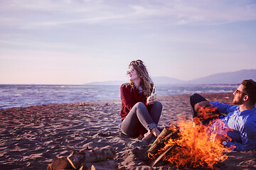 Image showing Young Couple Sitting On The Beach beside Campfire drinking beer