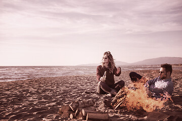 Image showing Young Couple Sitting On The Beach beside Campfire drinking beer