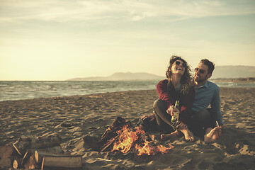 Image showing Young Couple Sitting On The Beach beside Campfire drinking beer