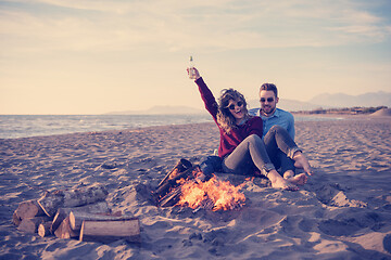 Image showing Young Couple Sitting On The Beach beside Campfire drinking beer