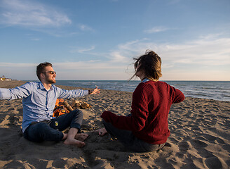 Image showing Young Couple Sitting On The Beach beside Campfire drinking beer