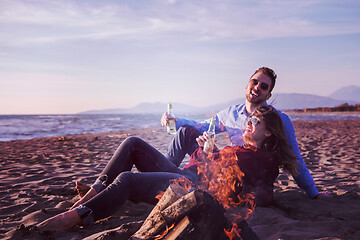 Image showing Young Couple Sitting On The Beach beside Campfire drinking beer