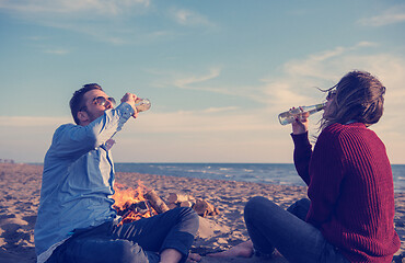 Image showing Young Couple Sitting On The Beach beside Campfire drinking beer